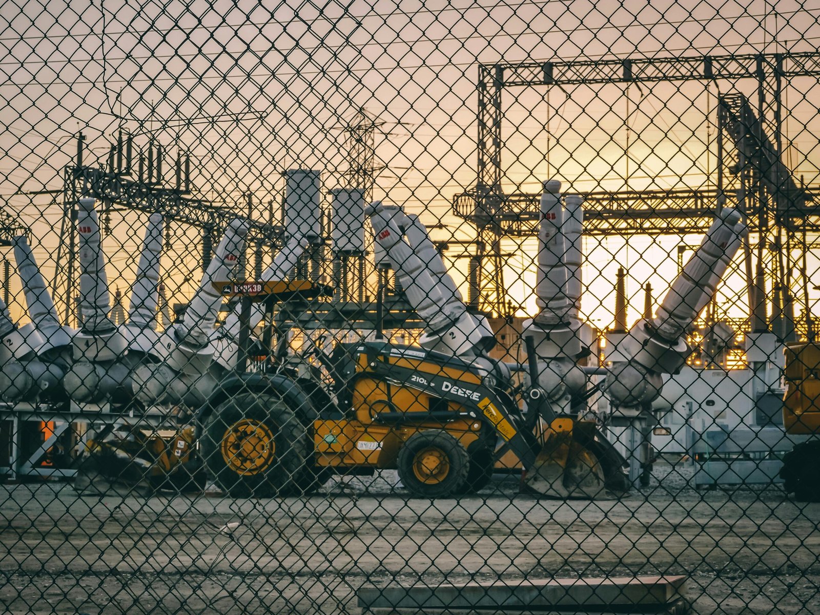 An industrial power plant with heavy machinery and equipment behind a chain link fence during sunset, showcasing energy infrastructure.