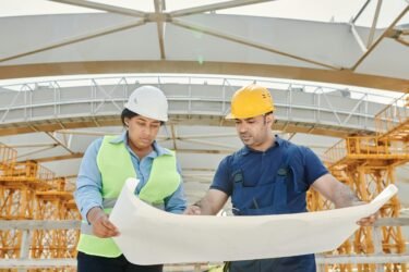 Male and female engineers discussing blueprints at a construction site, promoting teamwork and planning.